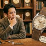 アンティーク時計店でロレックスのオイスターデイトを見つめ、「なぜ安いのか」と価格（¥300,000-¥500,000）や修理リスクについて悩んでいる日本人男性。