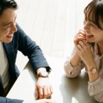 カフェで笑顔の日本人カップル。手元のコーチ腕時計（男性レザー、女性ピンクゴールド）が輝き、自信に満ちた様子。